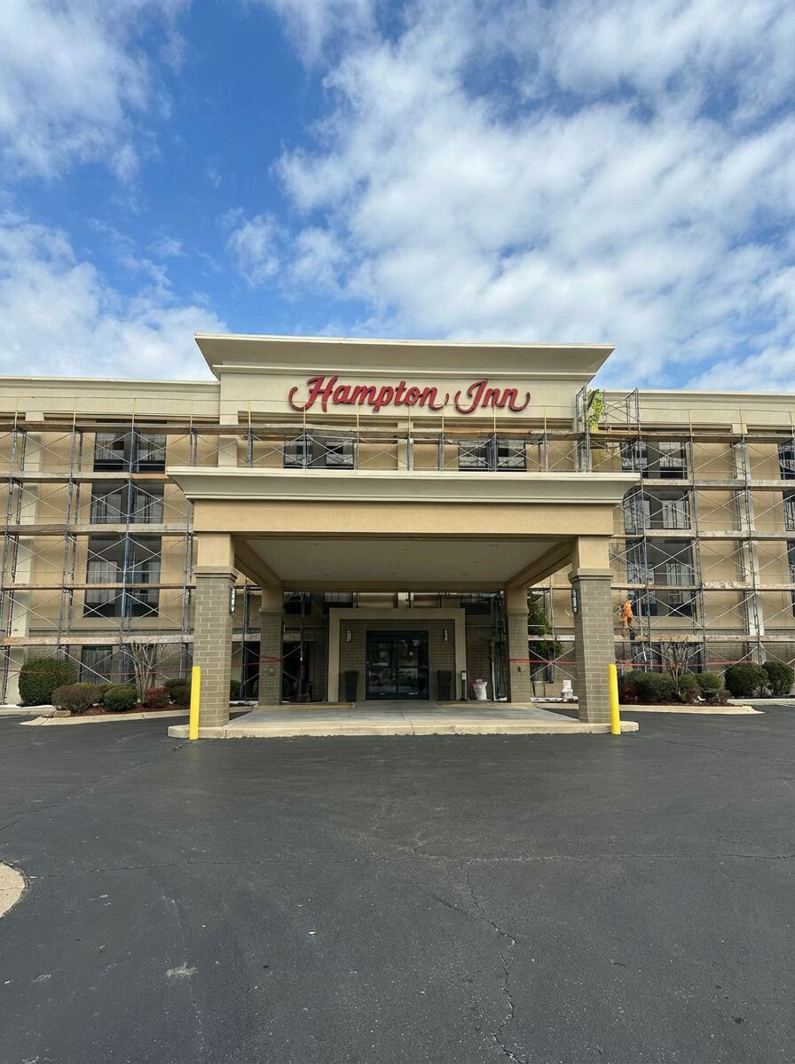 Exterior of Hampton Inn hotel with scaffolding on the side, showing the entrance and the hotel sign